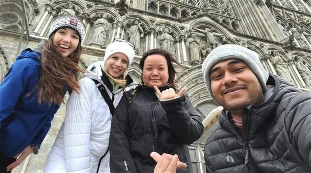 Fyra glada, unga människor står framför en kyrka iklädda ytterkläder. 